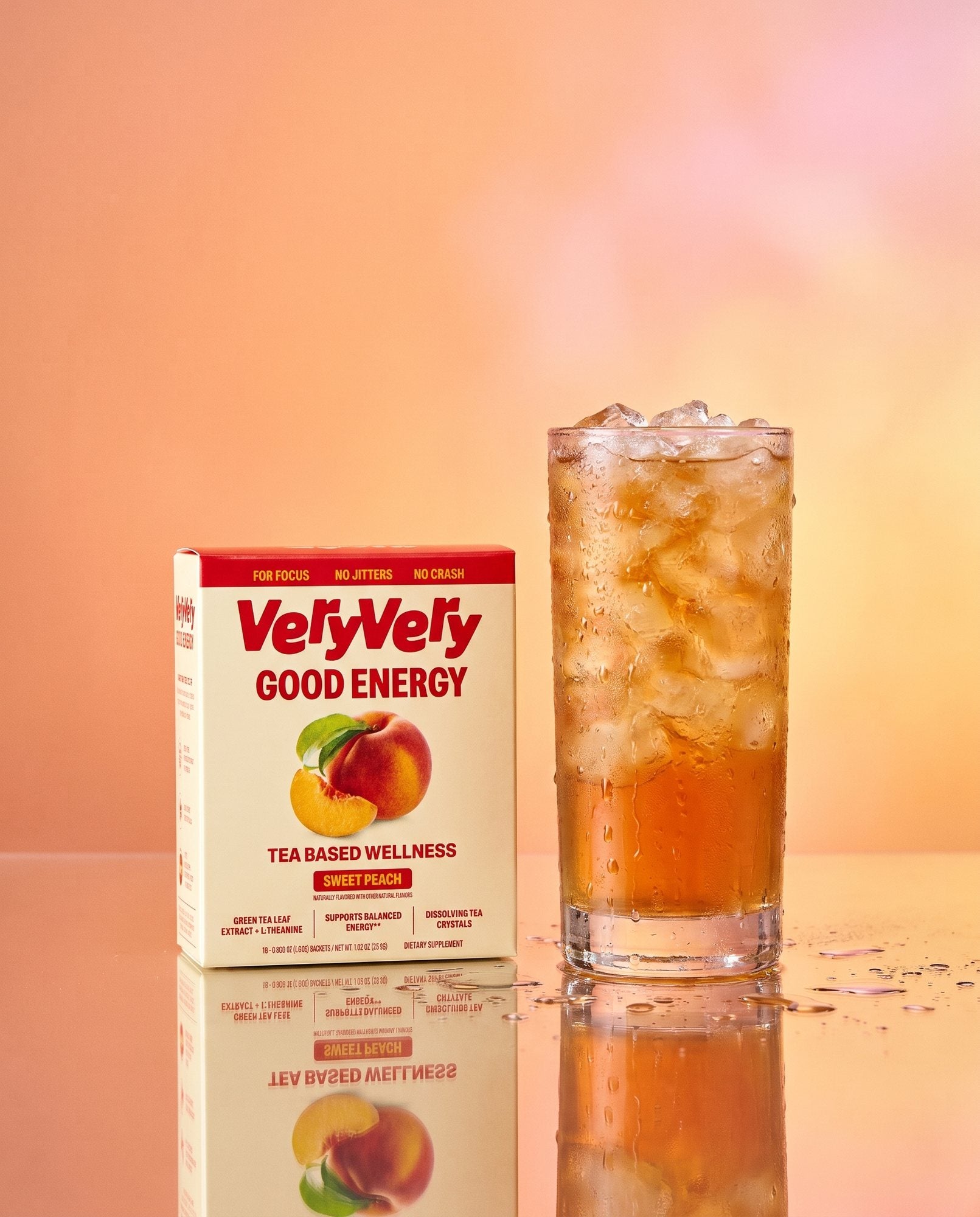 A box of VeryVery Good Energy beside a tall glass of peach iced tea